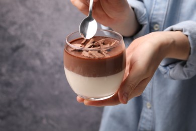 Photo of Woman holding glass with delicious panna cotta against grey background, closeup