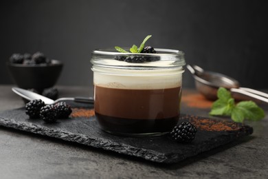 Photo of Tasty panna cotta with blackberries and mint in jar at grey table, closeup