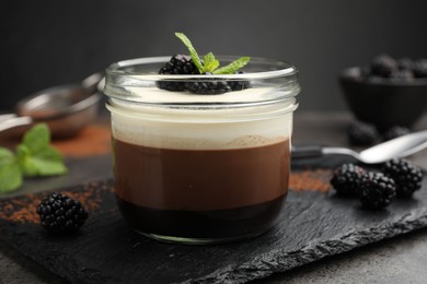 Photo of Tasty panna cotta with blackberries and mint in jar at grey table, closeup