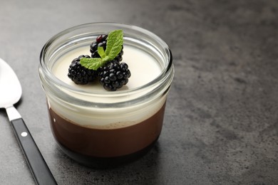 Photo of Tasty panna cotta with blackberries and mint in jar at grey table, closeup. Space for text