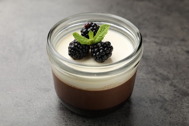 Photo of Tasty panna cotta with blackberries and mint in jar at grey table, closeup
