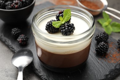 Photo of Tasty panna cotta with blackberries, mint and cocoa powder on grey table, closeup