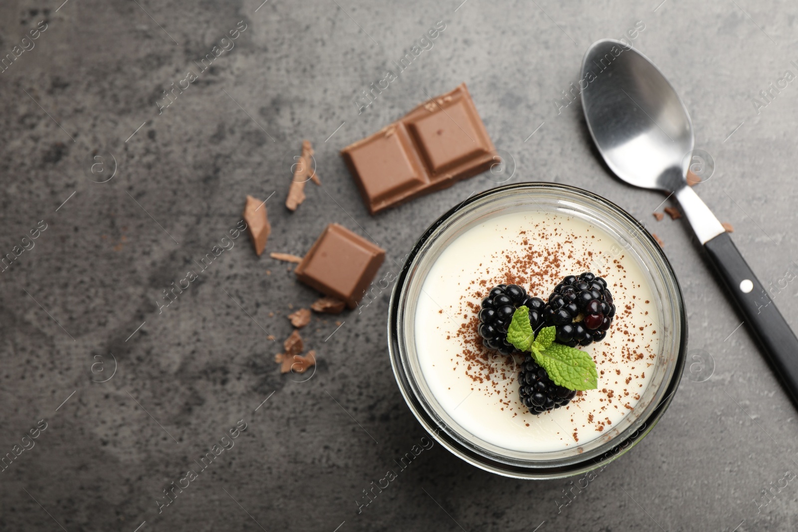 Photo of Tasty panna cotta with blackberries, mint and chocolate pieces on grey table, flat lay. Space for text