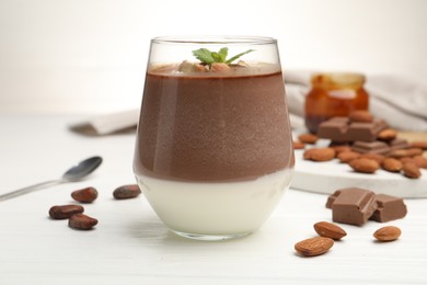 Photo of Delicious chocolate panna cotta with almonds, mint and cocoa beans on white wooden table, closeup