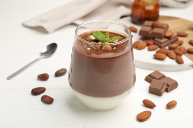 Photo of Delicious chocolate panna cotta with almonds, mint and cocoa beans on white wooden table, closeup