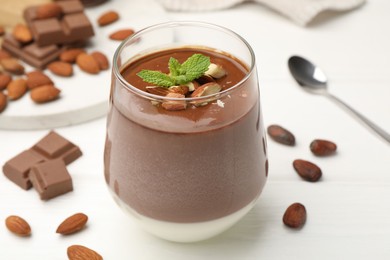 Photo of Delicious chocolate panna cotta with almonds, mint and cocoa beans on white wooden table, closeup