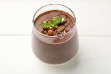 Photo of Delicious chocolate panna cotta with almonds and mint in glass on white table, closeup