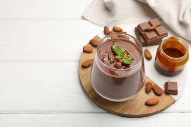 Photo of Delicious chocolate panna cotta with almonds, mint and caramel sauce on white wooden table. Space for text