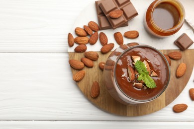Photo of Delicious chocolate panna cotta with almonds, mint and caramel sauce on white wooden table, flat lay. Space for text