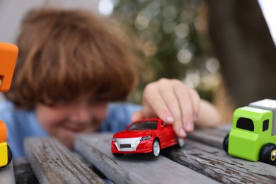 Photo of Little boy playing with toy cars on wooden bench outdoors, selective focus