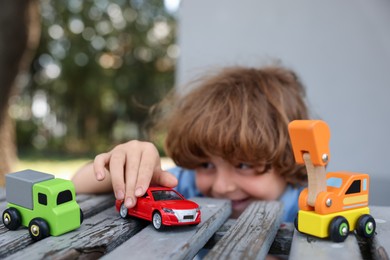 Photo of Little boy playing with toy cars on wooden bench outdoors, selective focus