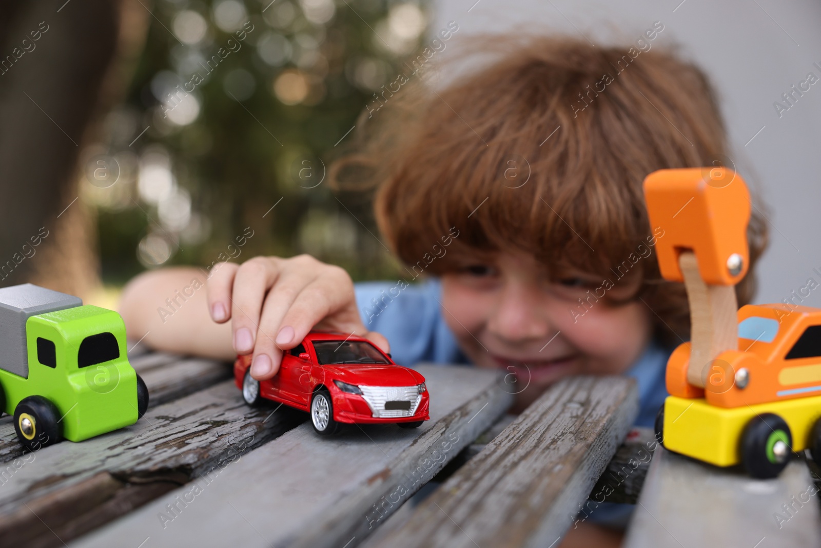 Little boy playing with toy cars on wooden bench outdoors, selective focus Photo of Little boy playing with toy cars on wooden bench outdoors, selective focus
