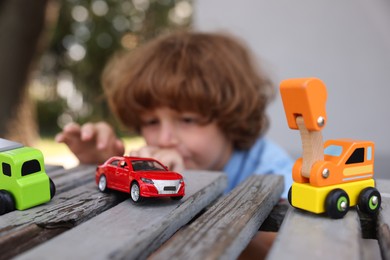 Photo of Little boy playing with toy cars on wooden bench outdoors, selective focus