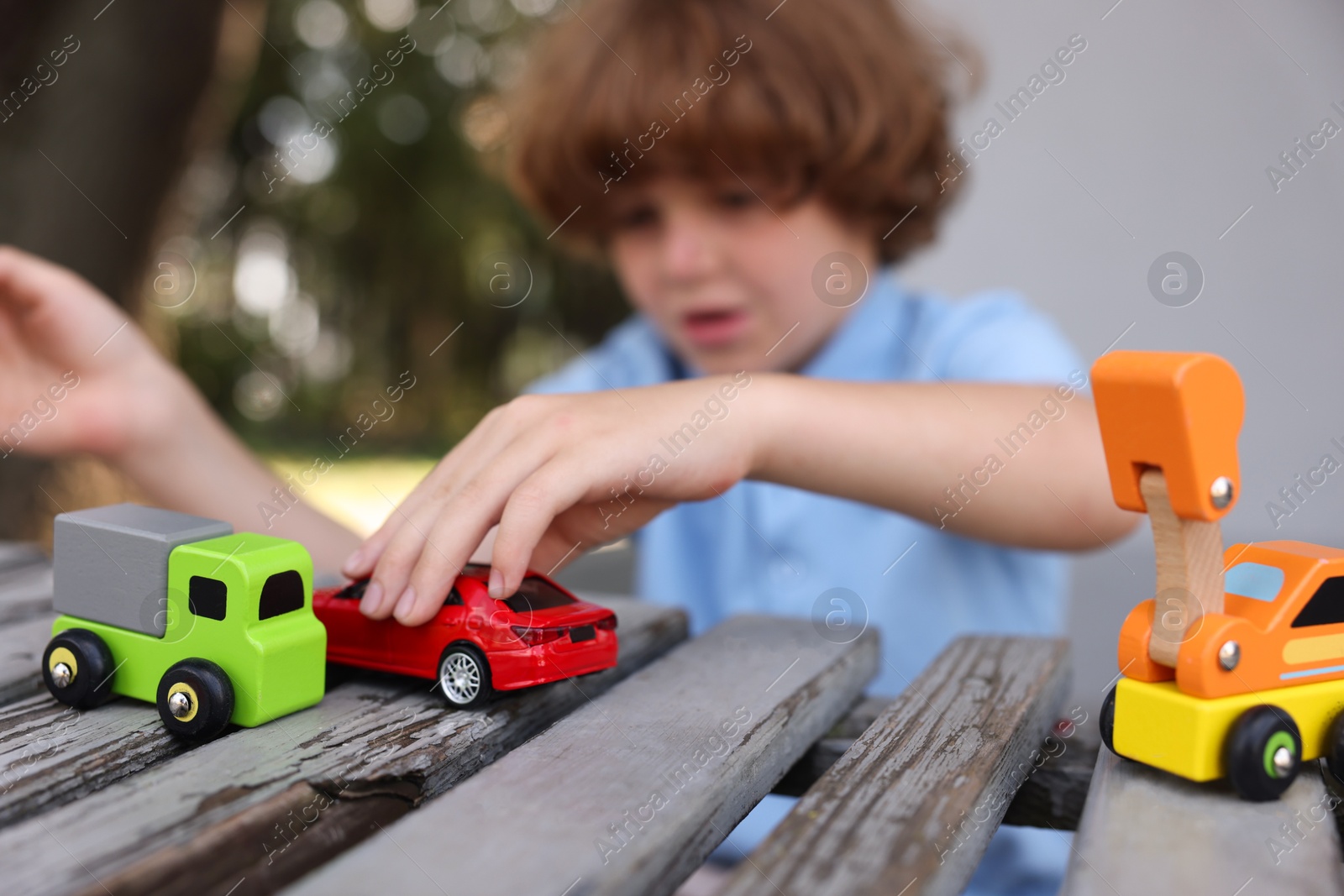 Little boy playing with toy cars on wooden bench outdoors, selective focus Photo of Little boy playing with toy cars on wooden bench outdoors, selective focus