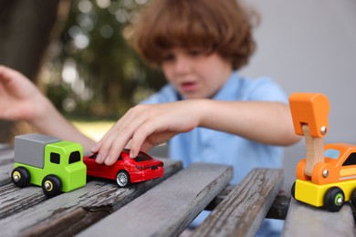 Photo of Little boy playing with toy cars on wooden bench outdoors, selective focus