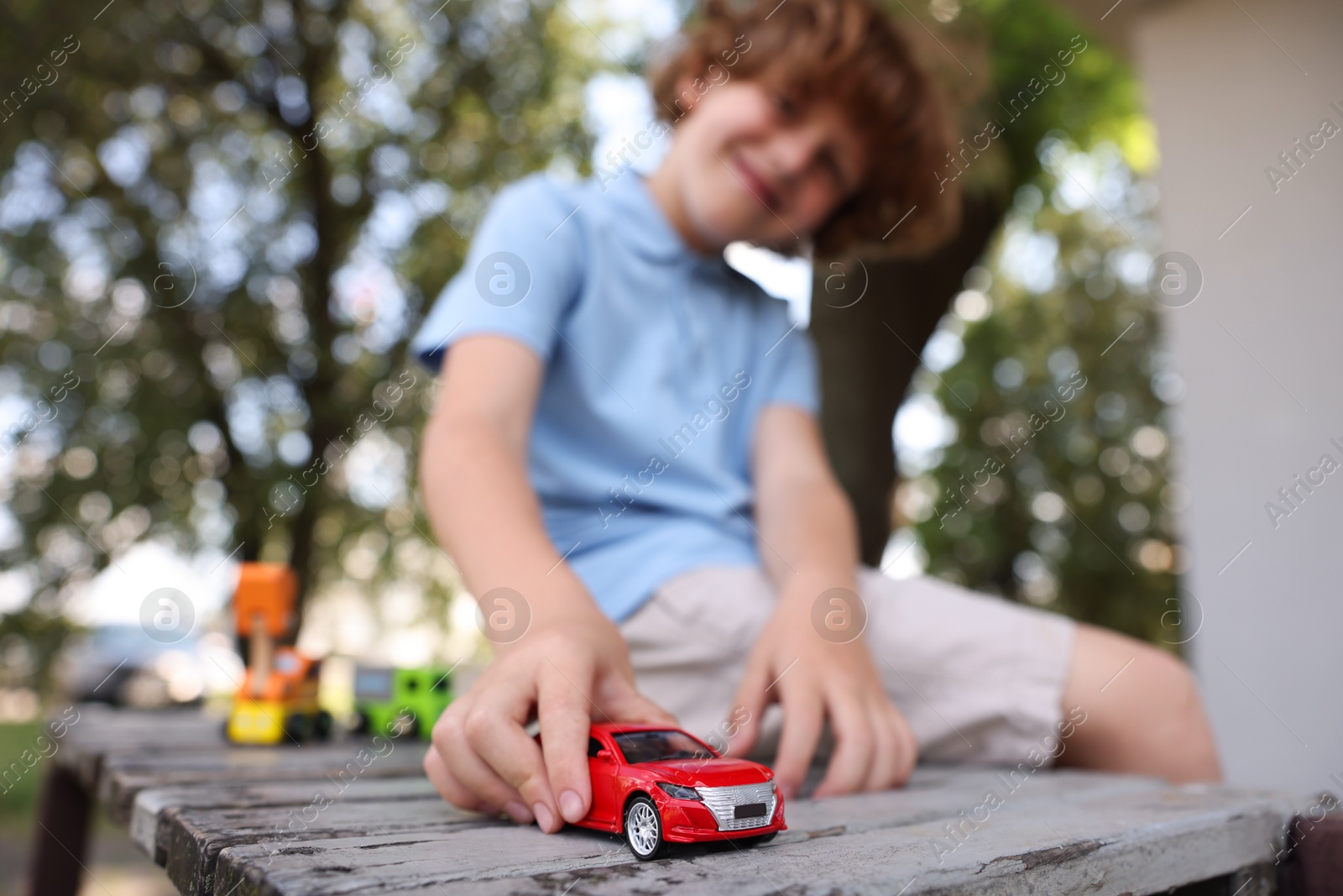 Little boy playing with toy car on wooden bench outdoors, selective focus Photo of Little boy playing with toy car on wooden bench outdoors, selective focus