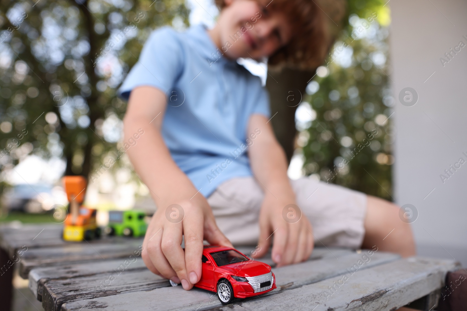 Little boy playing with toy car on wooden bench outdoors, selective focus Photo of Little boy playing with toy car on wooden bench outdoors, selective focus