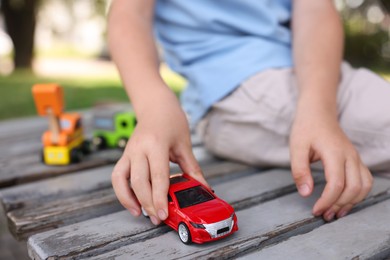Photo of Little boy playing with toy car on wooden bench outdoors, closeup