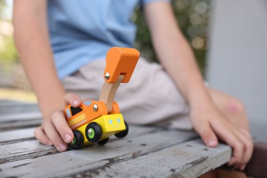 Photo of Little boy playing with toy car on wooden bench outdoors, closeup