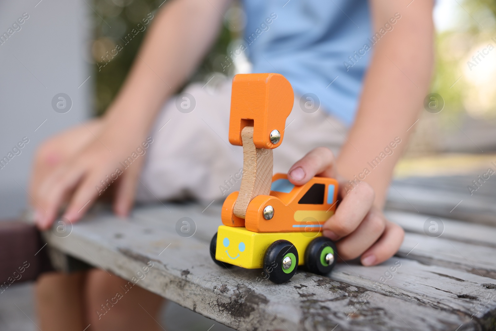 Photo of Little boy playing with toy car on wooden bench outdoors, closeup