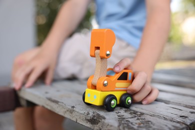 Photo of Little boy playing with toy car on wooden bench outdoors, closeup
