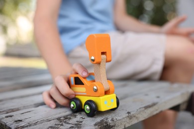 Photo of Little boy playing with toy car on wooden bench outdoors, closeup