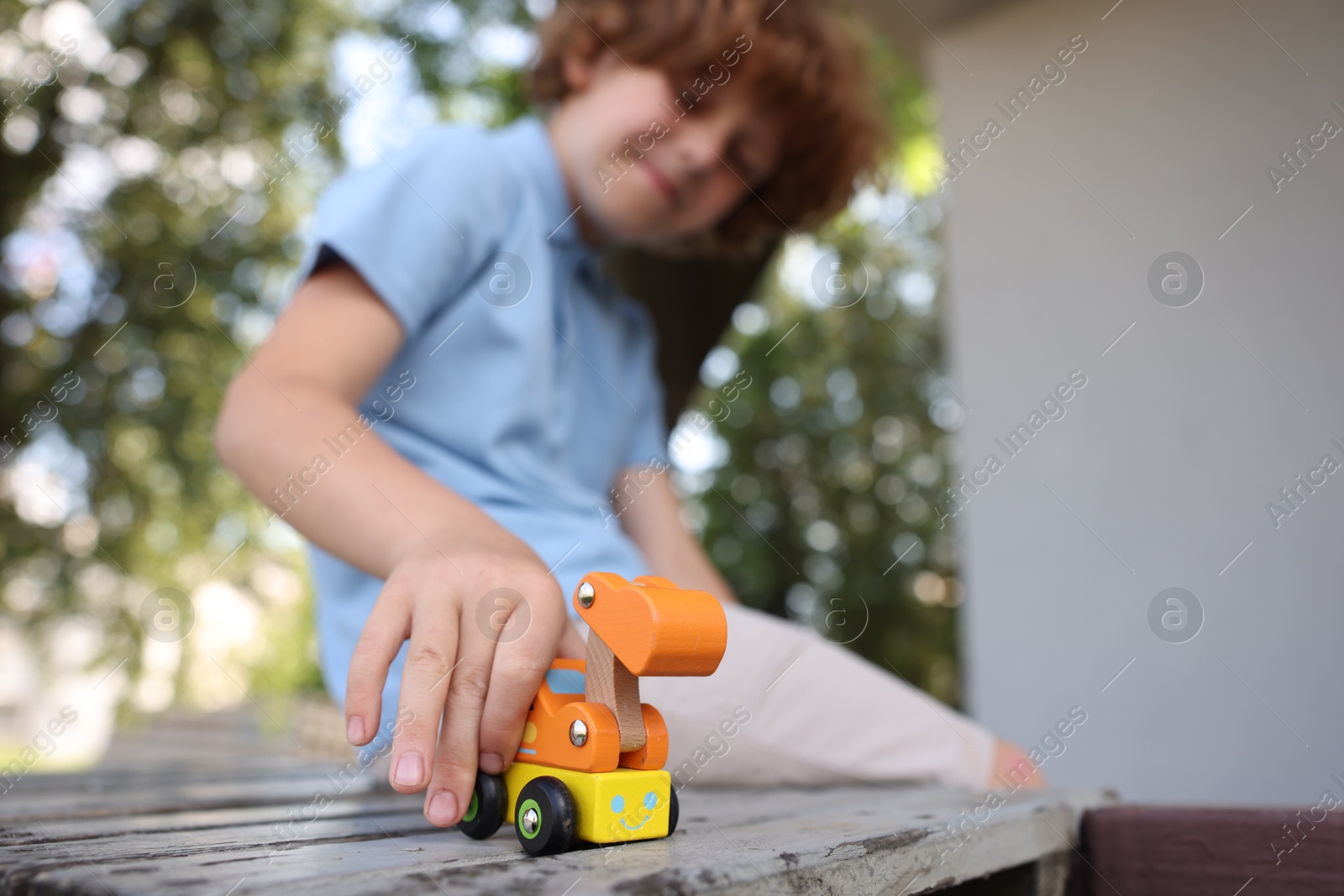 Little boy playing with toy car on wooden bench outdoors, selective focus Photo of Little boy playing with toy car on wooden bench outdoors, selective focus