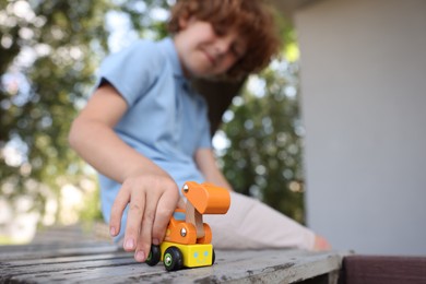 Photo of Little boy playing with toy car on wooden bench outdoors, selective focus