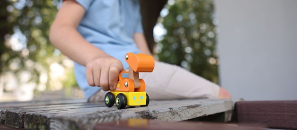 Photo of Little boy playing with toy car on wooden bench outdoors, closeup