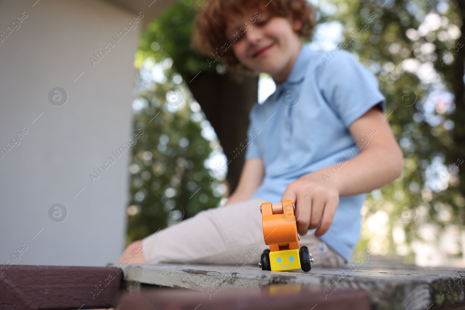 Little boy playing with toy car on wooden bench outdoors, selective focus Photo of Little boy playing with toy car on wooden bench outdoors, selective focus