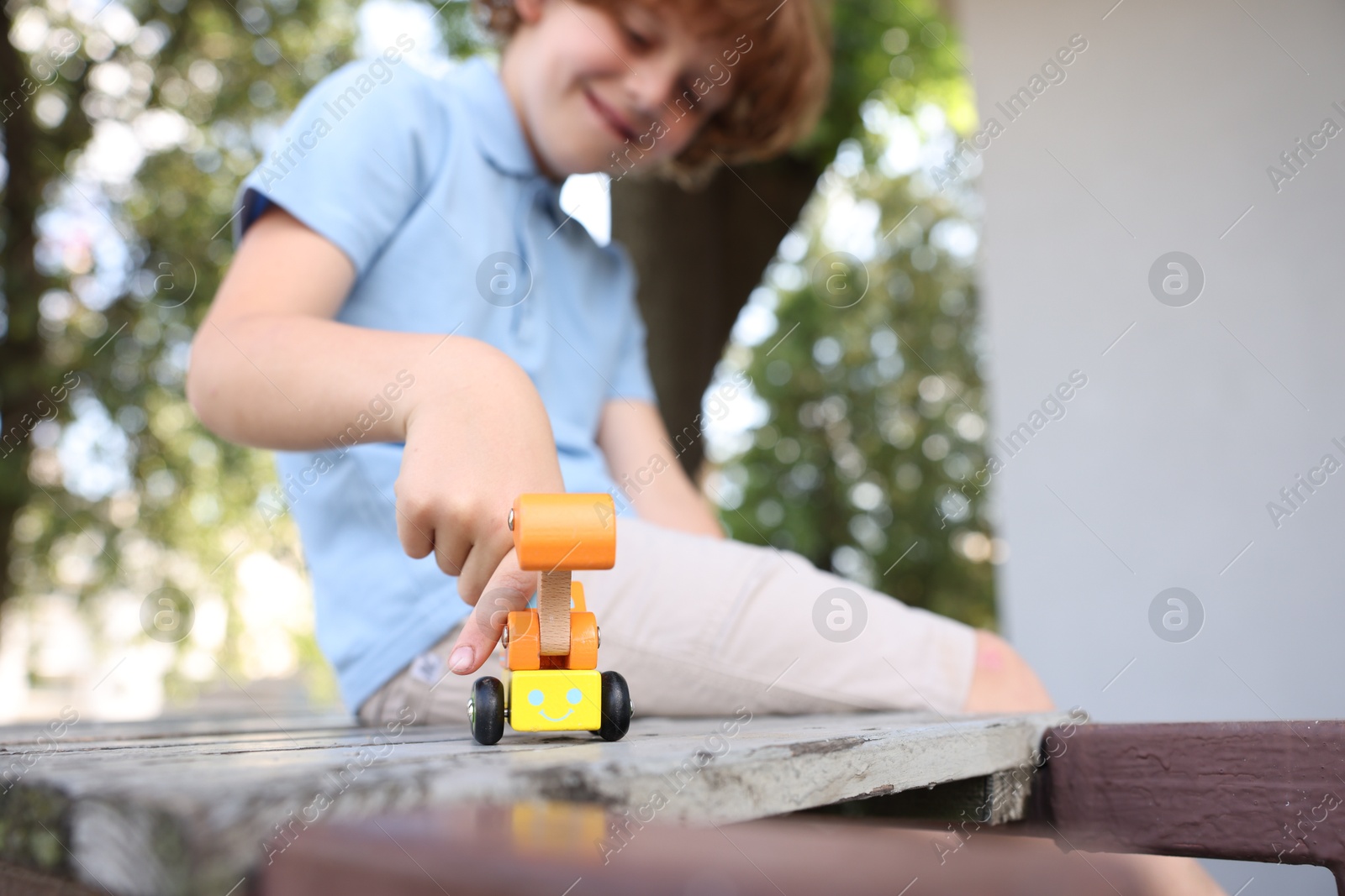 Little boy playing with toy car on wooden bench outdoors, selective focus Photo of Little boy playing with toy car on wooden bench outdoors, selective focus