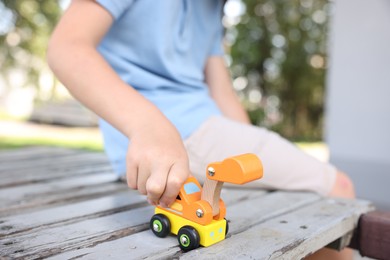 Photo of Little boy playing with toy car on wooden bench outdoors, closeup