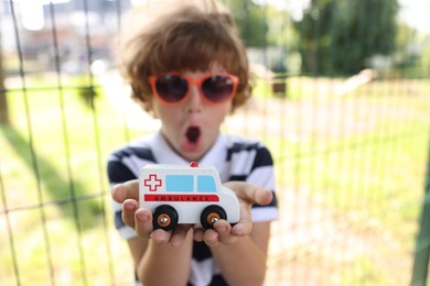 Photo of Surprised little boy with toy car outdoors, selective focus