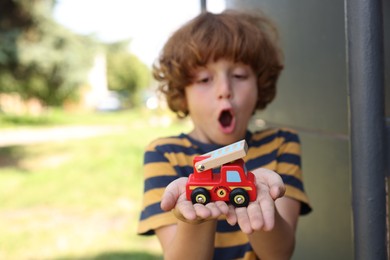 Photo of Surprised little boy with toy car outdoors, selective focus