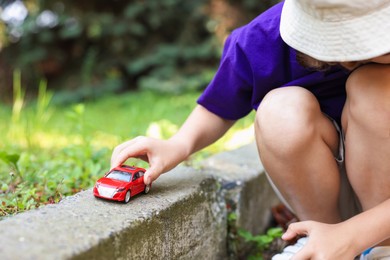 Photo of Little boy playing with toy car outdoors, closeup