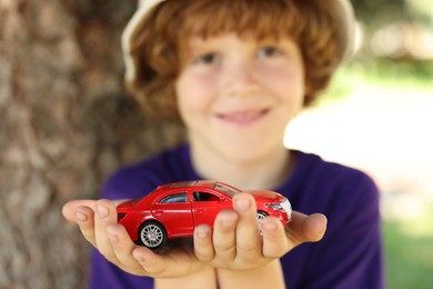 Photo of Little boy with toy car outdoors, selective focus