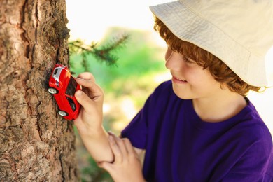 Photo of Little boy playing with toy car near tree outdoors