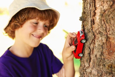 Photo of Little boy playing with toy car near tree outdoors, selective focus