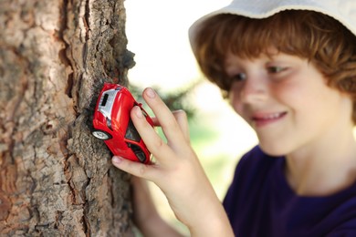 Photo of Little boy playing with toy car near tree outdoors, selective focus