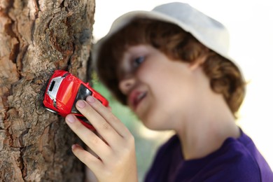Photo of Little boy playing with toy car near tree outdoors, selective focus