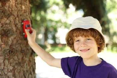 Photo of Little boy playing with toy car near tree outdoors