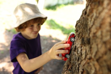 Photo of Little boy playing with toy car near tree outdoors, selective focus