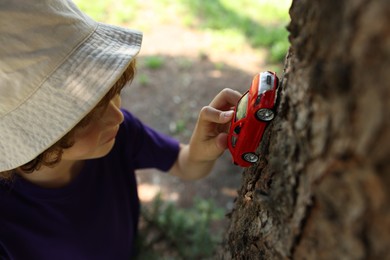 Photo of Little boy playing with toy car near tree outdoors