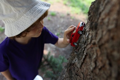 Photo of Little boy playing with toy car near tree outdoors