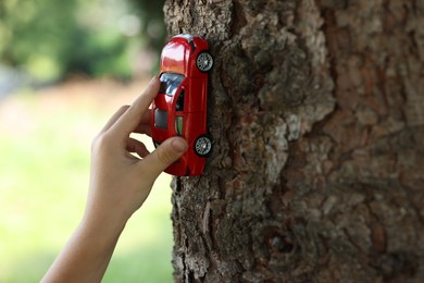 Photo of Little boy playing with toy car near tree outdoors, closeup