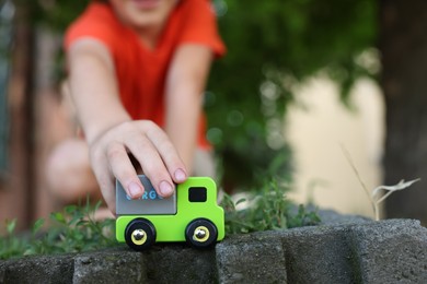 Photo of Little boy playing with toy car outdoors, closeup. Space for text