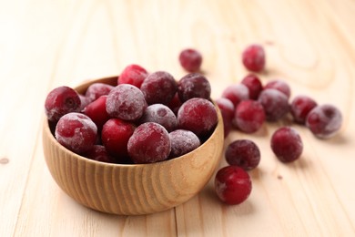 Photo of Ripe frozen cherries and bowl on light wooden table, closeup