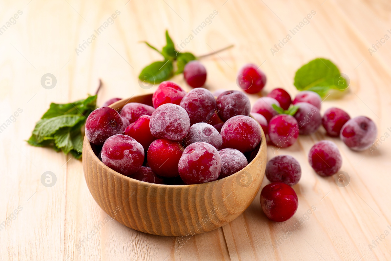 Photo of Ripe frozen cherries and bowl on light wooden table, closeup