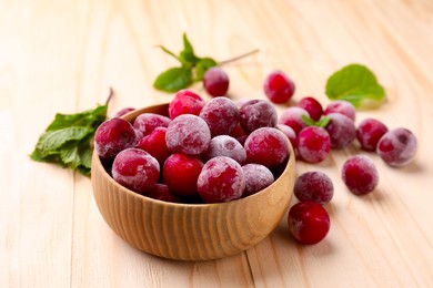 Photo of Ripe frozen cherries and bowl on light wooden table, closeup