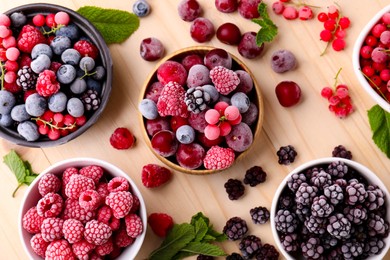 Photo of Different ripe frozen berries and mint leaves on light wooden table, flat lay